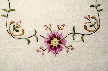 Part of the embroidered corner from the border with a pinkish-red flower and buds on wavy branches...