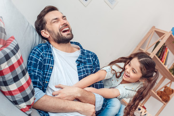 Father and little daughter at home lying girl tickling father laughing cheerful
