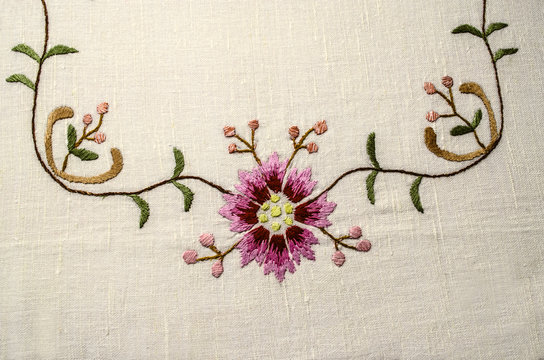 Part of the embroidered corner from the border with a pinkish-red flower and buds on wavy branches with small leaves
