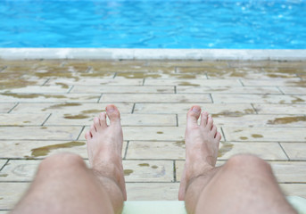 Hairy legs of a man against a background of pure blue water in a pool. A tired man finally relaxed by the water. The concept of the long-awaited holiday. All inclusive. Sunbathe.