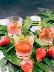 Homemade Strawberry liqueur on a metal table. Alcoholic fruit cocktail shots in a glasses. Green leafs