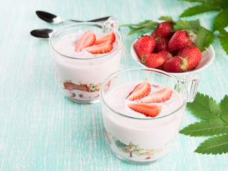 Bowl with fresh strawberry yogurt. Diet yoghurt and granola with slice of berries in a glass on a wooden table. Copy space