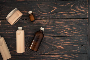 Bottles with spa cosmetic products from above on dark brown wood table. Beauty blogger, salon treatments concept. Minimalism, copyspace