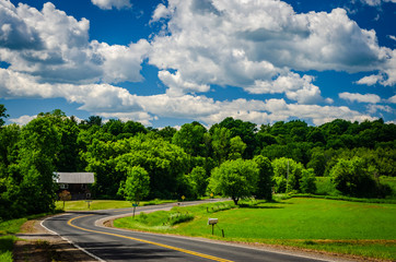Countryside road curving past a small barn into a treed area