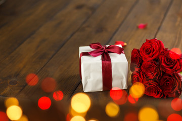 Red roses and gift box on brown wooden table. Bokeh rings effect