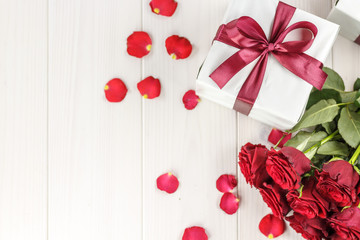 Red roses and gift box on white wooden table, top viewed