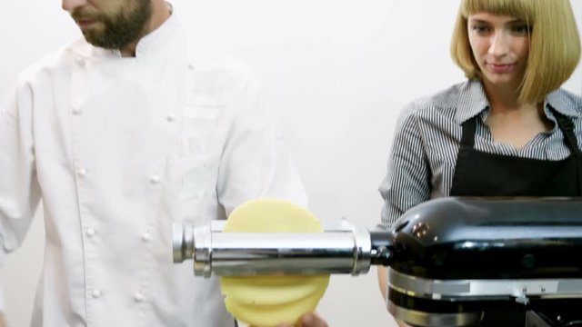 Chef showing blonde woman how to make macaroni using the pasta machine. 4K