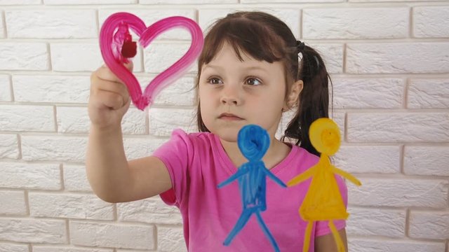 The child is drawing. A little girl draws a heart with colors. A child draws parents.