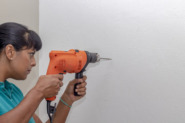 Latin woman drilling wall. She is empowered but the drill has a life of its own