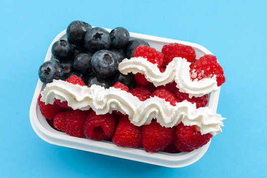 Independence day, happy fourth of july and sweet dessert concept with close up on the american flag made of raspberries, blueberries and whipped cream, isolated on minimalist blue background