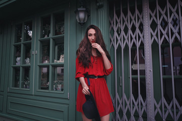 Elegant brunette young woman wearing red dress and straw hat on the street cafe. Fashion and style.