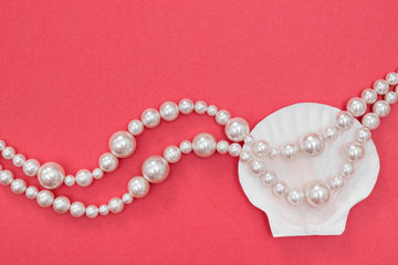Pearl necklace and seashell on pink background
