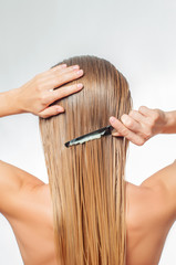 Blond woman with long wet hair is applying hair conditioner