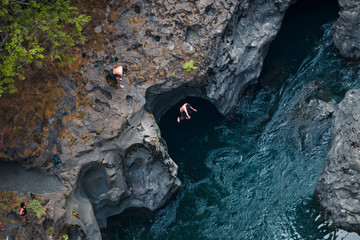 Boys Jumping Off A Rock Cliff Into The Blue Mountain Waters In Washington
