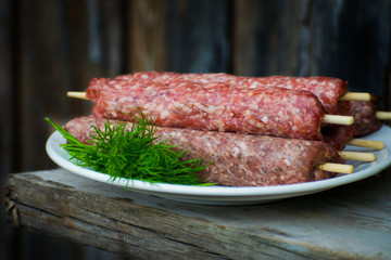 Raw lulya kebab from meat on a white plate and wooden board with with dill.