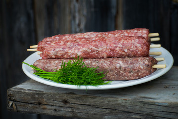 Raw lulya kebab from meat on a white plate and wooden board with with dill.