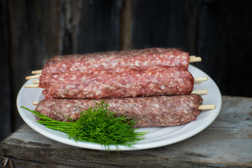 Raw lulya kebab from meat on a white plate and wooden board with with dill.