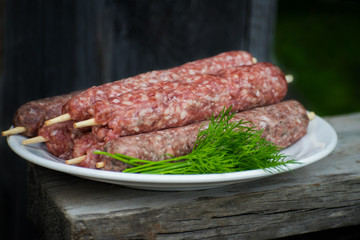 Raw lulya kebab from meat on a white plate and wooden board with with dill.