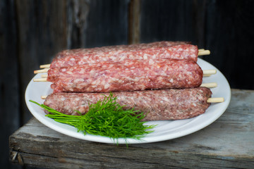 Raw lulya kebab from meat on a white plate and wooden board with with dill.