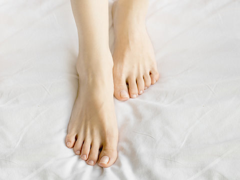 female legs in bed view from above, white bedding.