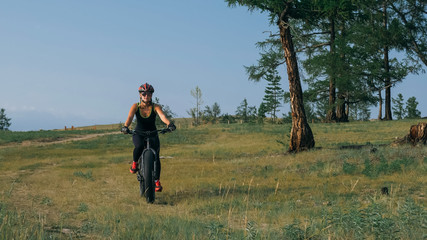 Fat bike also called fatbike or fat-tire bike in summer riding in the forest. Beautiful girl and her bicycle in the forest. She rolls her bike and poses to the operator.