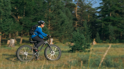 Fat bike also called fatbike or fat-tire bike in summer riding in the forest. The guy rides a bicycle among trees and stumps. He overcomes some obstacles on a bumpy road.