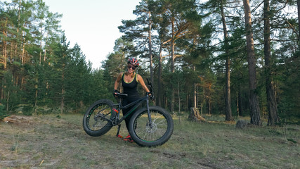 Obraz premium Fat bike also called fatbike or fat-tire bike in summer riding in the forest. Beautiful girl and her bicycle in the forest. She rolls her bike and poses to the operator.