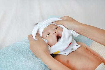 Cute asian infant baby boy lying on bed and mother while put on some clothes to her baby after bath.