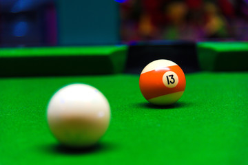 Billiard ball in a green pool table focus on the number thirteen orange and white ball