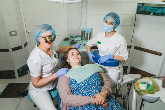 Woman at dentist clinic gets dental treatment to fill a cavity in a tooth. Dental restoration and composite material polymerization with UV light and laser. The patient, the Doctor and the assistant