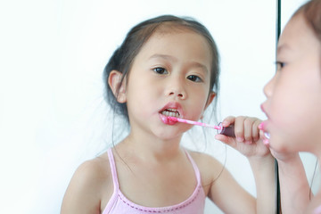 Cute little Asian child girl trying lip gloss near a mirror.
