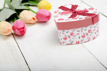 High angle shot of pink rosy and yellow Spring tulip flowers and gift box on white wooden table