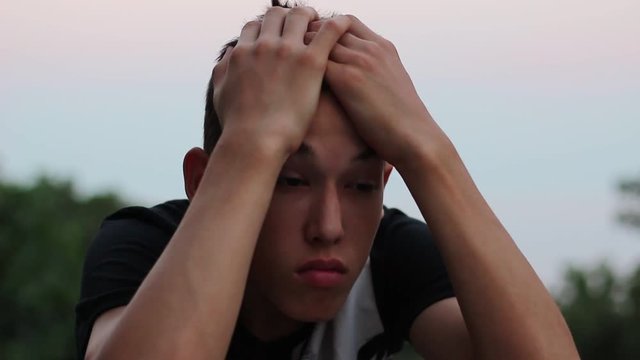 Depressed Young Man Portrait at Sunset. Teen Boy Sits Alone Looking Sad Or Worried. Beautiful summer sunset