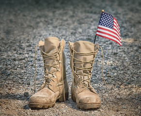 Old military combat boots with the American flag. Rocky gravel background. Memorial Day or Veterans...