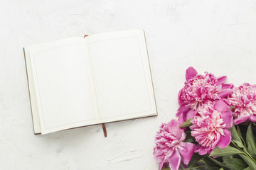 Pink peonies and an open diary on a light stone background. Flat lay, top view