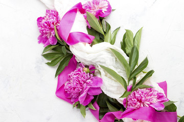 Pink peonies wrapped in a white fabric with a pink ribbon on a light stone background