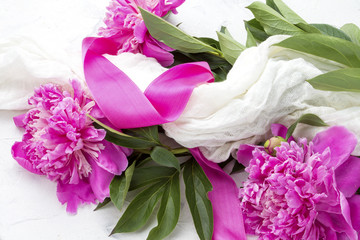 Pink peonies wrapped in a white fabric with a pink ribbon on a light stone background