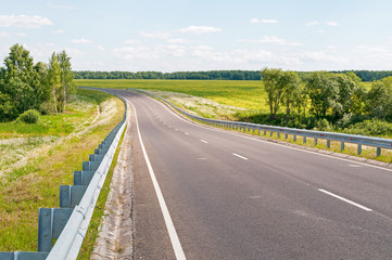 Steep highway turn with metal rails along against blossoming meadow and forest background. Kaluzhsky region, Russia.