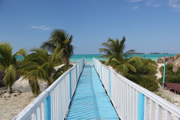 Wooden bridge that leads to the beach with palm trees, on the island of Cuba