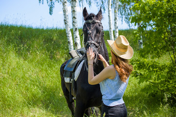 Woman enjoying horse company. Young Beautiful Woman in straw hat With black Horse Outdoors, stylish girl at american country style 