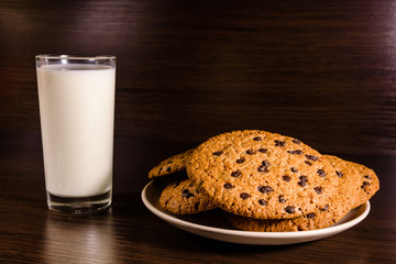 Plate with chocolate chip cookies and a glass of milk on a dark wooden table