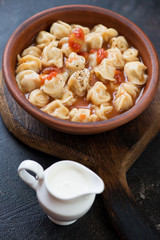 Soup with meat dumplings pelmeni served in a clay bowl with a jar of sour cream, vertical shot, selective focus