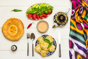 traditional Uzbek dish Manta with potatoes, meat and pumpkin, Uzbek ж, tomatoes and cucumbers on plates with national ornaments on a white wooden background