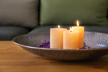 Fototapeta na wymiar Plate with burning wax candles, water and flower petals on wooden table