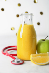 Bottle of tasty smoothie with fresh fruits and stethoscope on table. Health care concept