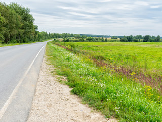Fototapeta na wymiar Vanishing straight highway along sunny meadow. Kaluzhsky region, Russia.