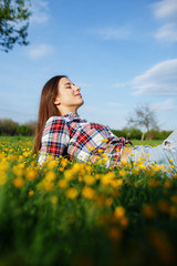 Naklejka na ściany i meble Beautiful smiling woman in plaid shirt and jeans lying on a grass outdoor. Beautiful woman lying down in the meadow of flowers. Pretty girl relaxing outdoors on spring grass