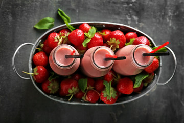 Basket with bottles of tasty smoothie and strawberries on grey table