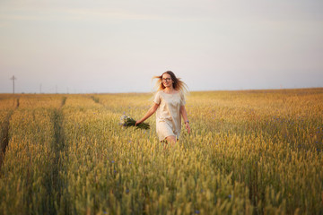 girl with flowers walking on a grain field.