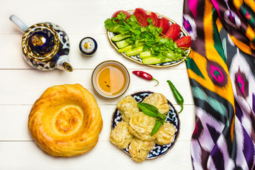 traditional Uzbek dish Manta with potatoes, meat and pumpkin, Uzbek ж, tomatoes and cucumbers on plates with national ornaments on a white wooden background